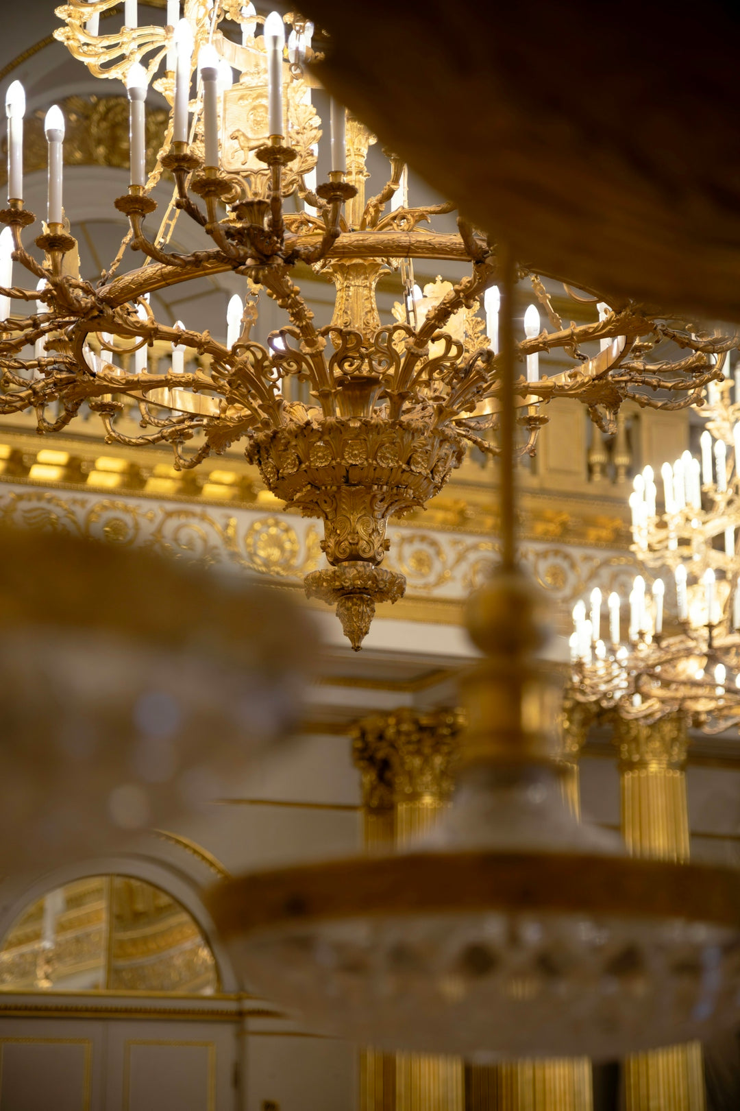Ornate golden chandeliers illuminate a grand interior.