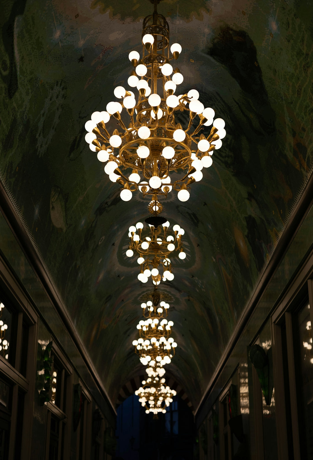 Row of ornate chandeliers hanging from a decorated ceiling.