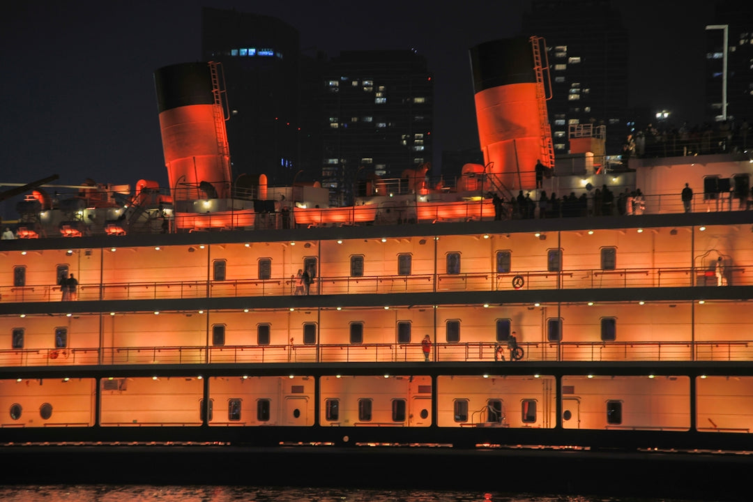 Large illuminated ship docked at night with city lights.