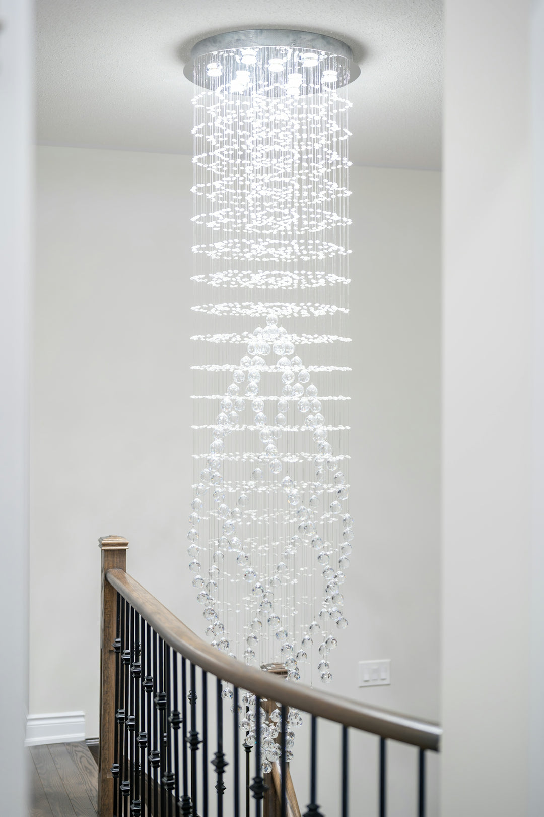A long, sparkling crystal chandelier hangs over a staircase.