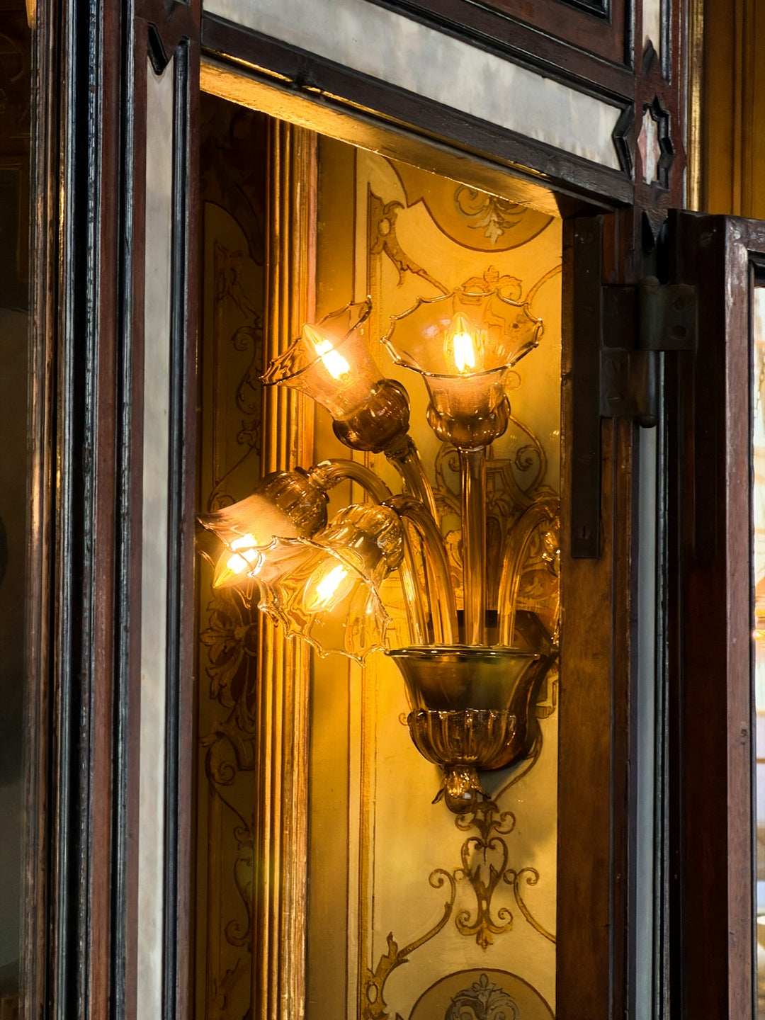 An ornate antique wall sconce with glowing bulbs.