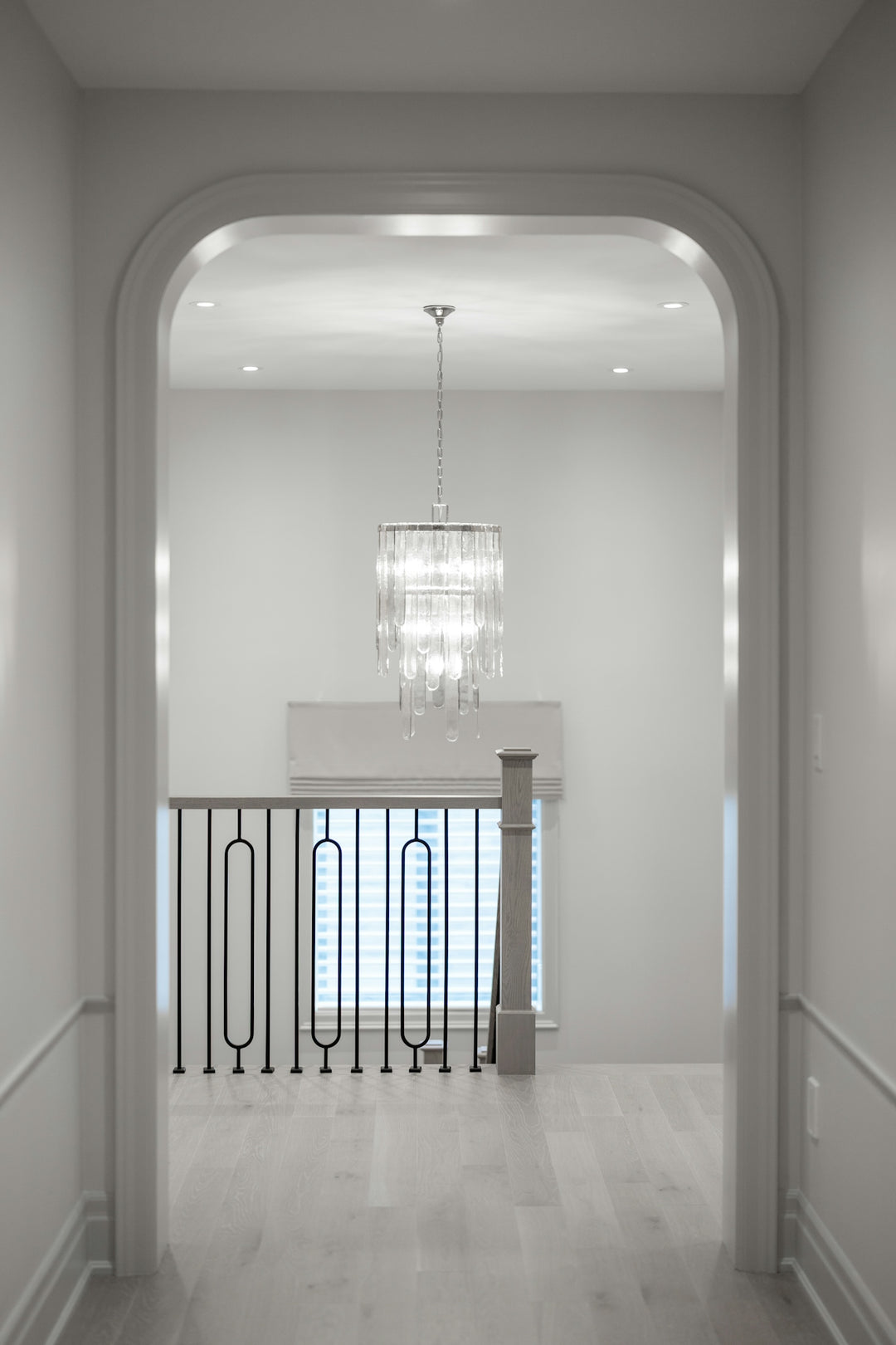 Arched doorway leads to hallway with modern chandelier and railing.