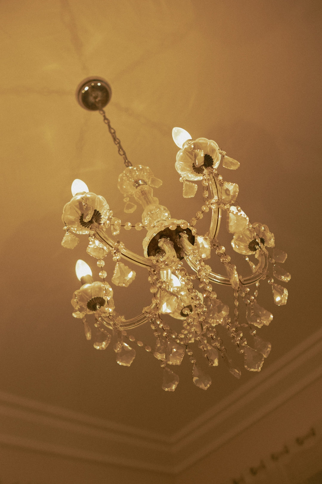 A crystal chandelier hangs from a ceiling, illuminated warmly.