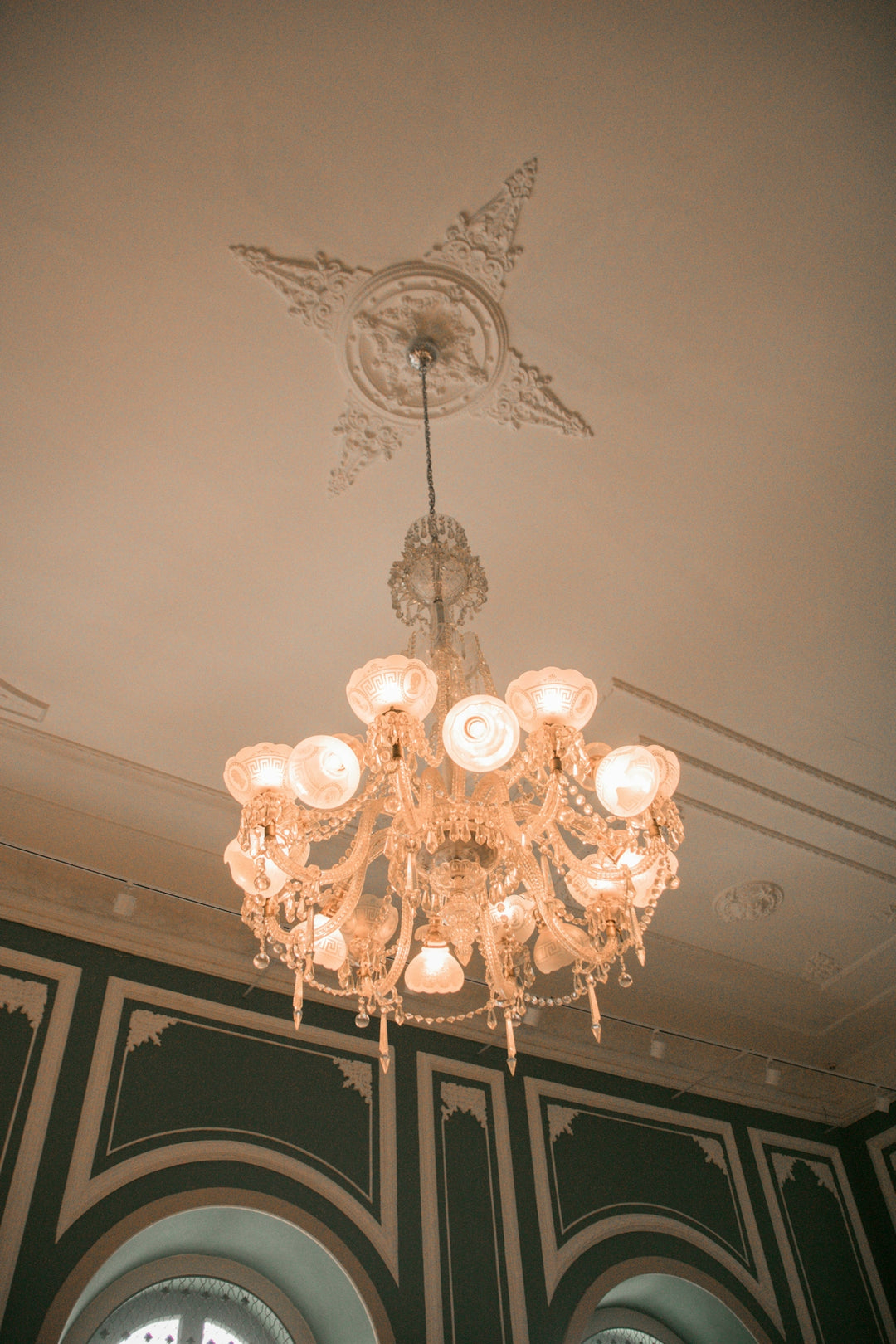 A luxurious chandelier hangs from an ornate, decorated ceiling.