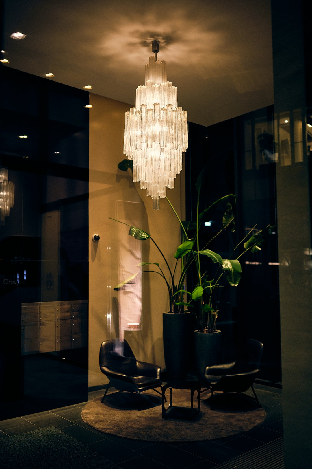 Elegant chandelier brightens a stylish lobby with chairs and plants.
